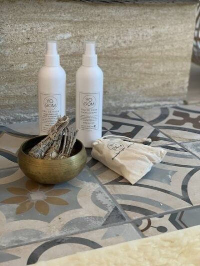 Sprays nettoyants pour tapis de yoga et sprays d'ambiance . 2 flacons posés sur un tapis de yoga avec un bol chantant. Marque Yogom