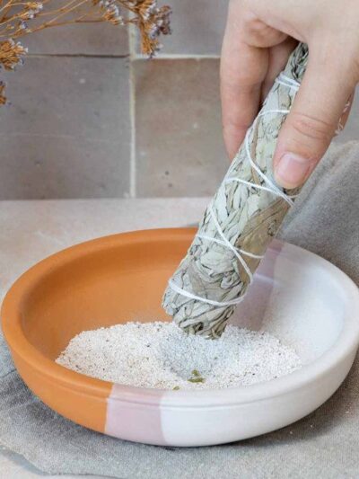 Tresse baton de sauge blanche allumée au-dessus d'une assiette porte-encens