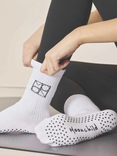 Femme qui met des chaussettes de pilates antidérapantes blanches avec picots noirs sur la semelle et logo moonchild