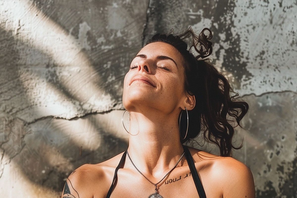 Une femme aux cheveux blonds en bataille, ornée d'un collier, se tient dans un cadre intérieur rustique et ensoleillé, dégageant une ambiance sereine.