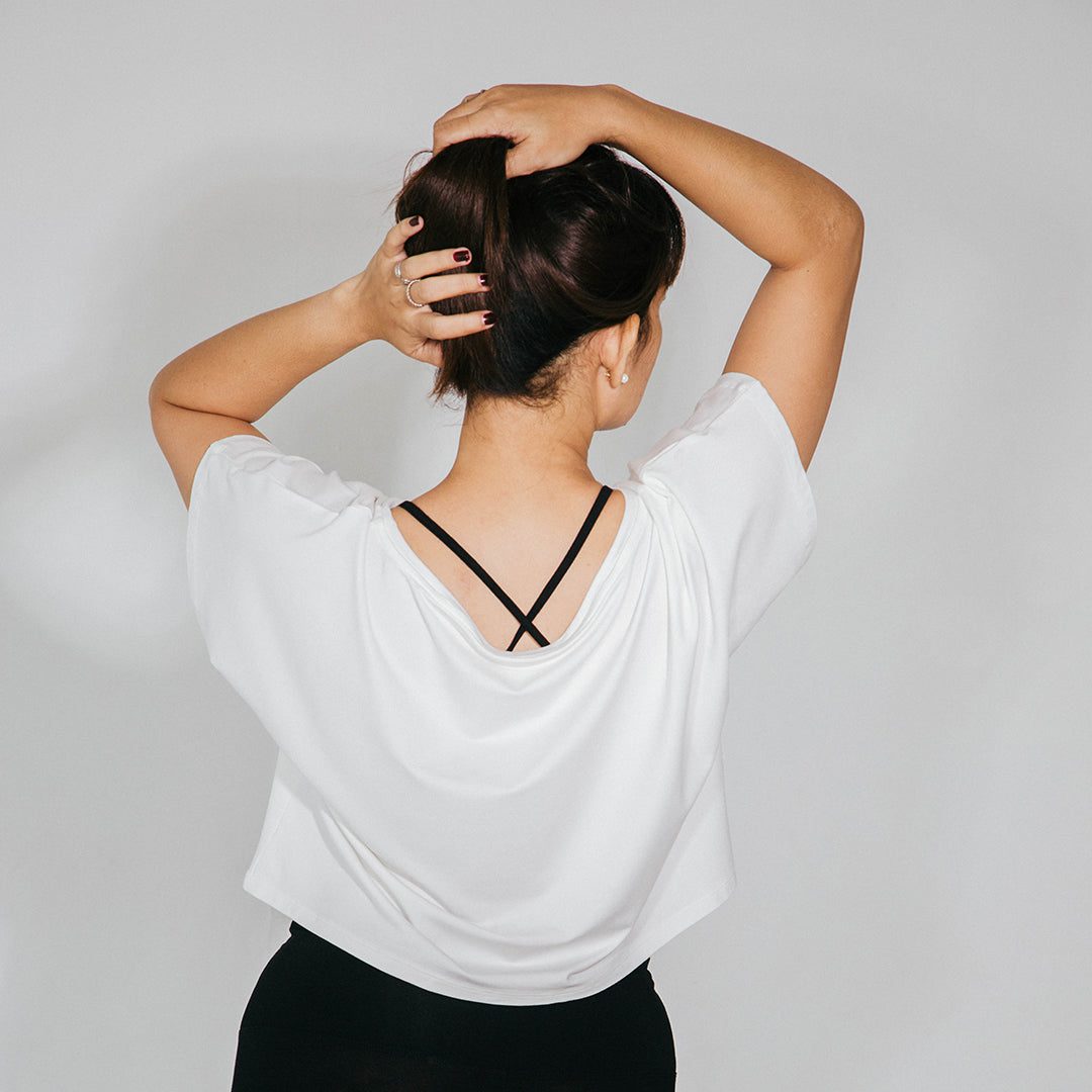 Femme vue de dos qui porte un top yoga ample avec dos dégagé et brassière noire à bretelles croisées dans le dos