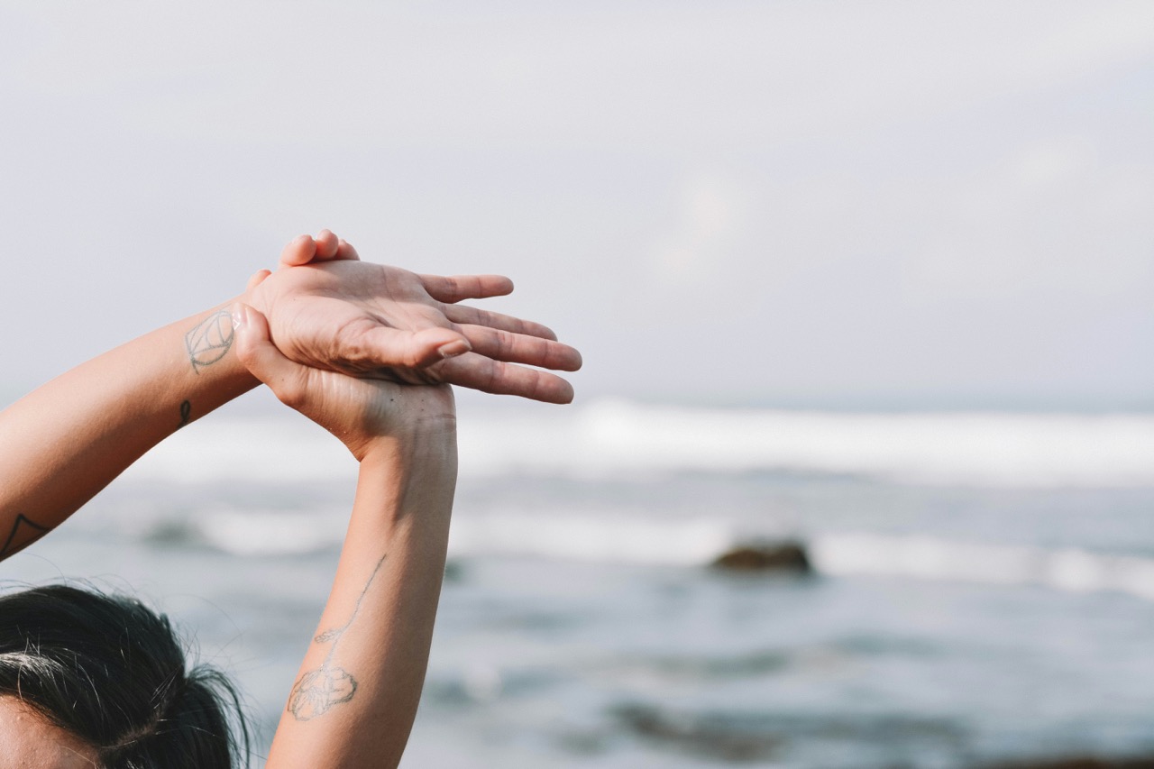Mains tatouées levées devant la mer en posture de yoga debout de demi-lune