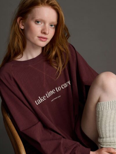 Femme aux cheveux longs roux qui porte un sweat-shirt bordeaux avec inscription blanche devant